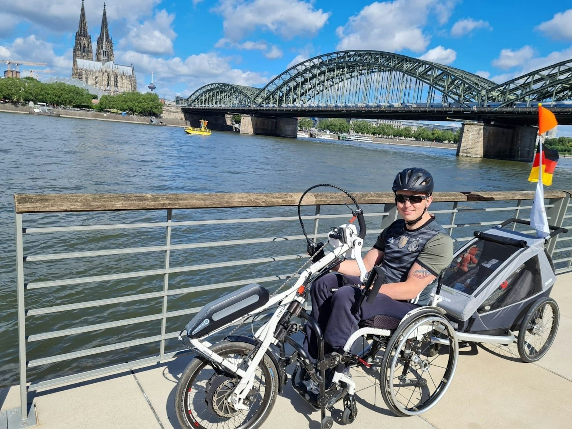 Ein Mann im Rollstuhl (Handbike) steht am Rheinufer in Köln
