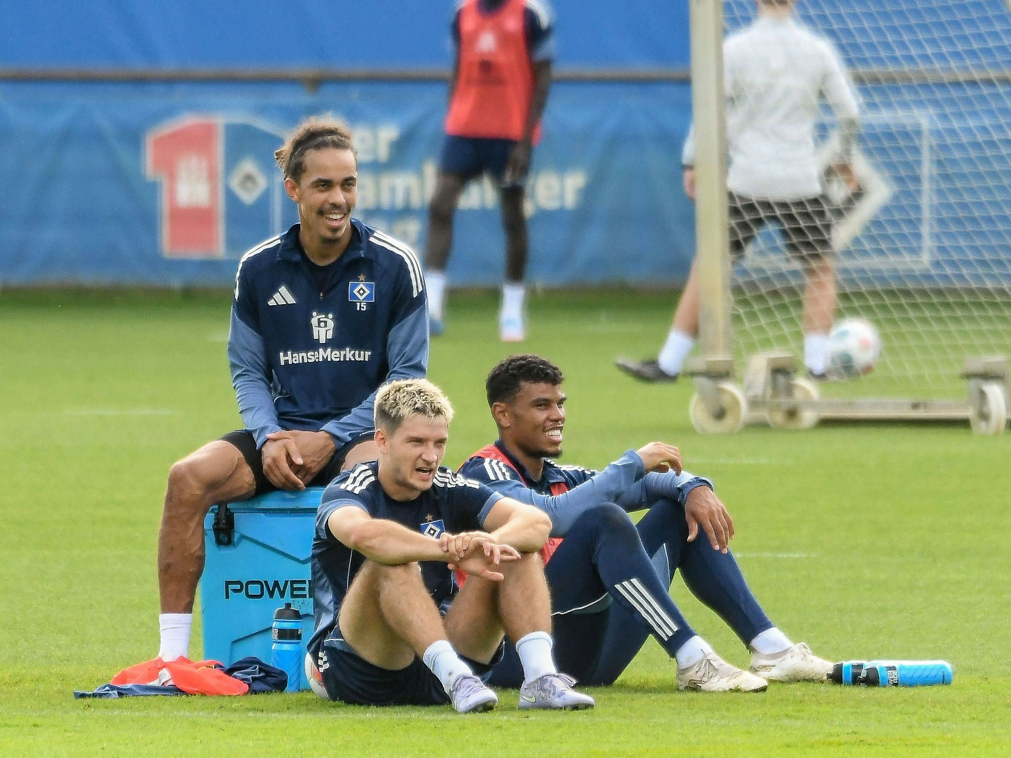 Yussuf Poulsen, Noah Katterbach und Ransford-Yeboah Königsdörffer sitzen während des Trainings auf dem Boden und gucken sich etwas an.