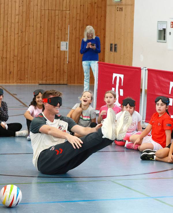 Marius Bülter (1. FC Köln) hatte am 23. September 2025 so seine Probleme beim Blindenfußball-Workshop mit Kollege Dominique Heintz (l.) und zahlreichen Kindern in Porz.