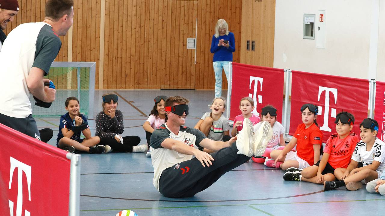 Marius Bülter (1. FC Köln) hatte am 23. September 2025 so seine Probleme beim Blindenfußball-Workshop mit Kollege Dominique Heintz (l.) und zahlreichen Kindern in Porz.