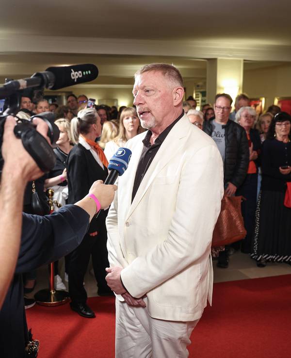 Boris Becker trägt einen weißen Anzug und gibt auf dem roten Teppich ein Interview und wird dabei von mehreren Kameras gefilmt.