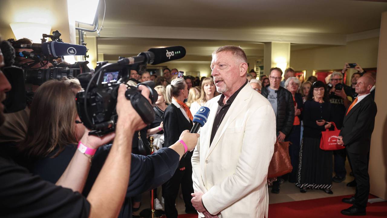 Boris Becker trägt einen weißen Anzug und gibt auf dem roten Teppich ein Interview und wird dabei von mehreren Kameras gefilmt.
