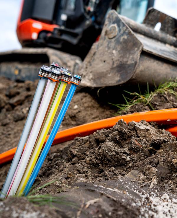 Glasfaser-Kabel liegen auf einer Baustelle, freigelegt von einem Bagger.