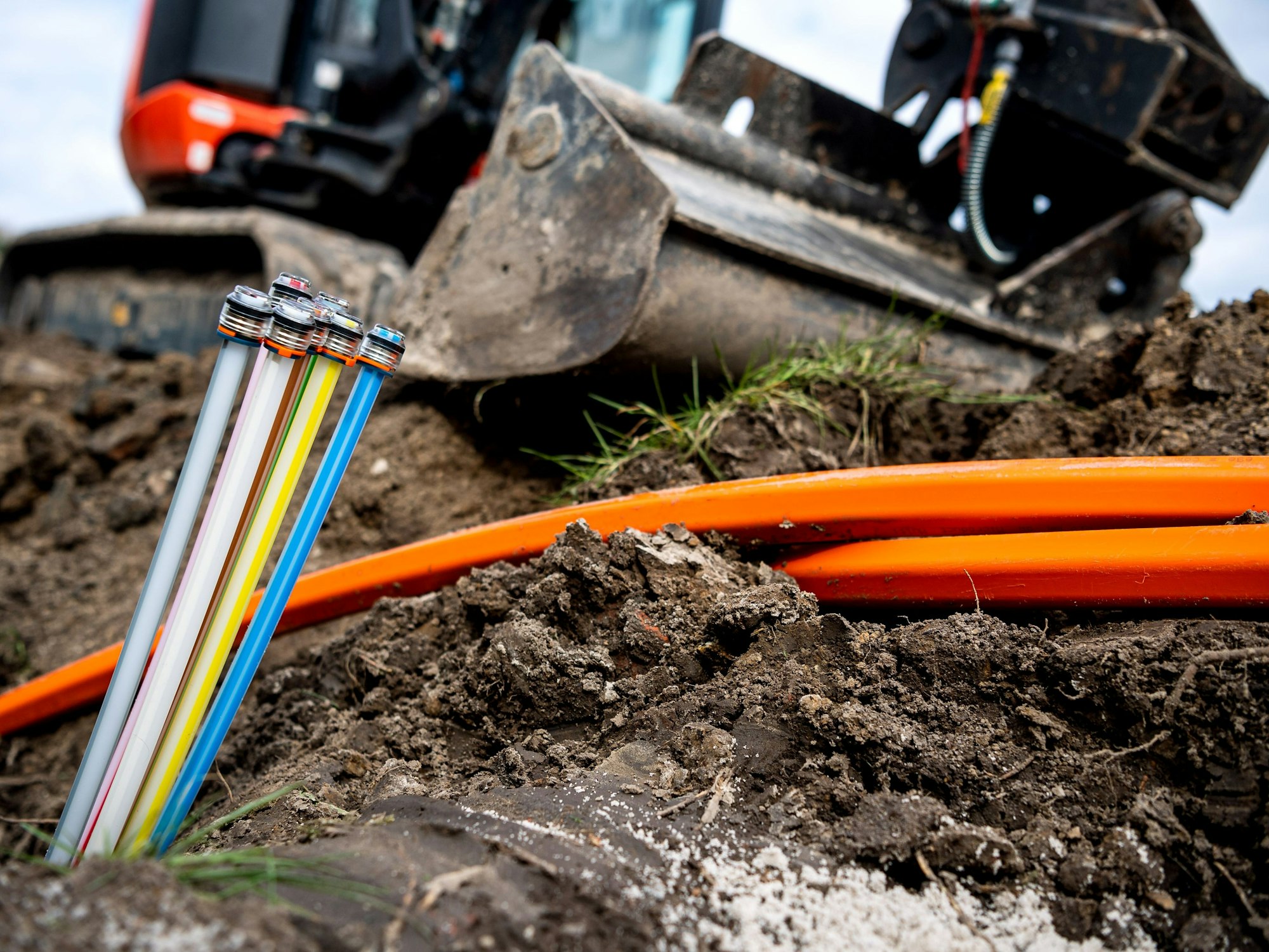 Glasfaser-Kabel liegen auf einer Baustelle, freigelegt von einem Bagger.