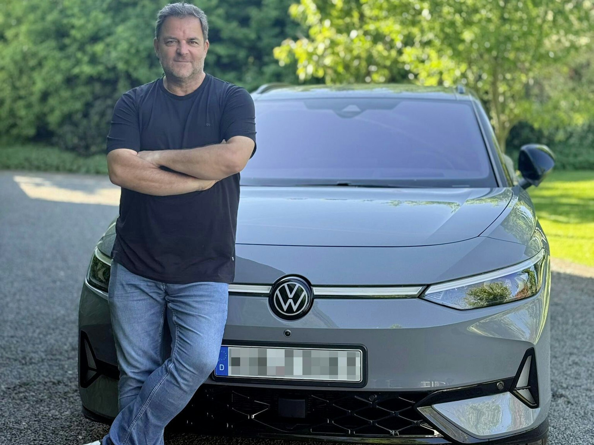 Ein Mann in Jeans und T-Shirt lehnt an einem grauen VW mit Elektromotor