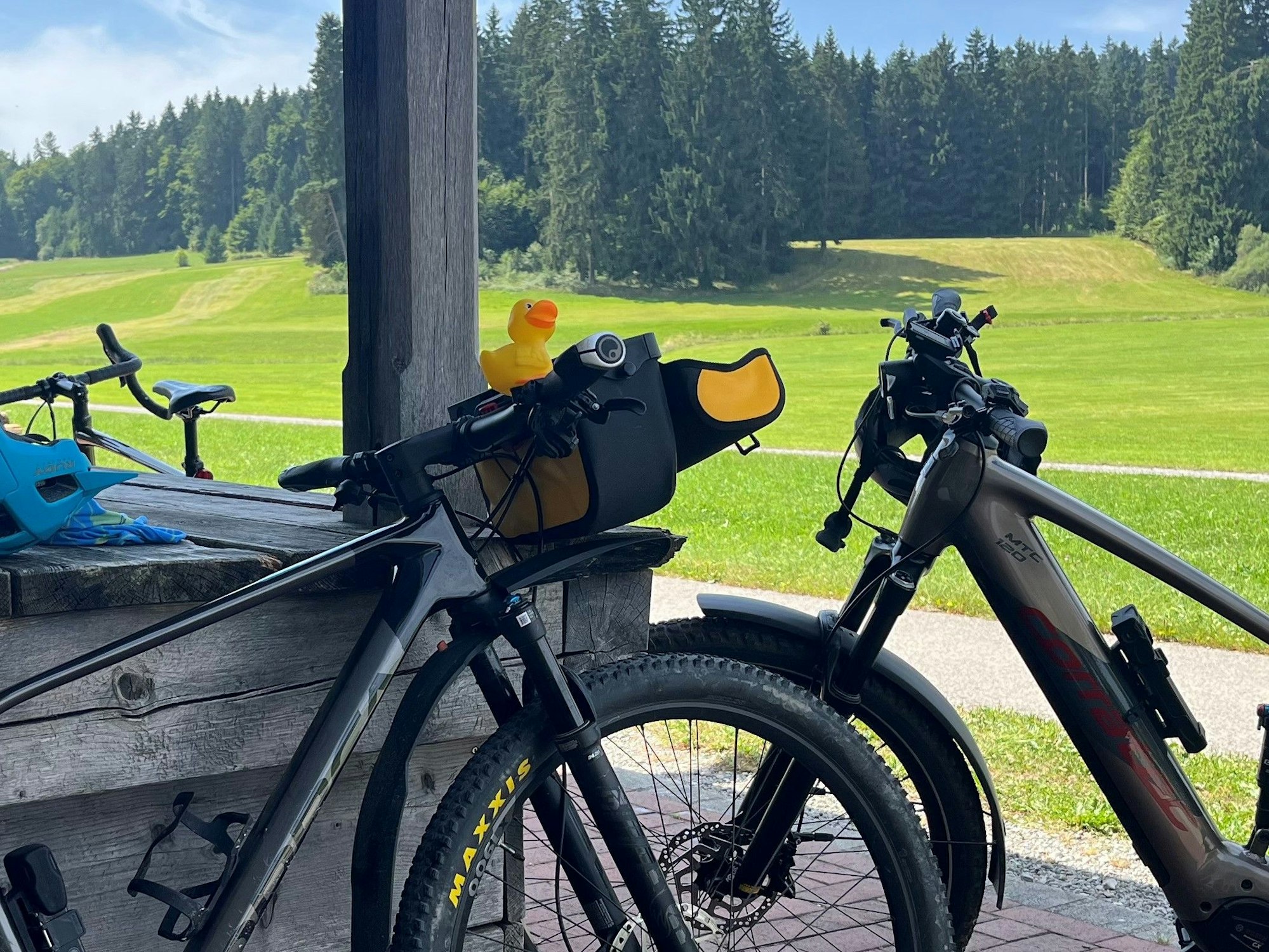 Fahrräder lehnen an einem Holzstadl, im Hintergrund ein Nadelwald auf einer Anhöhe.