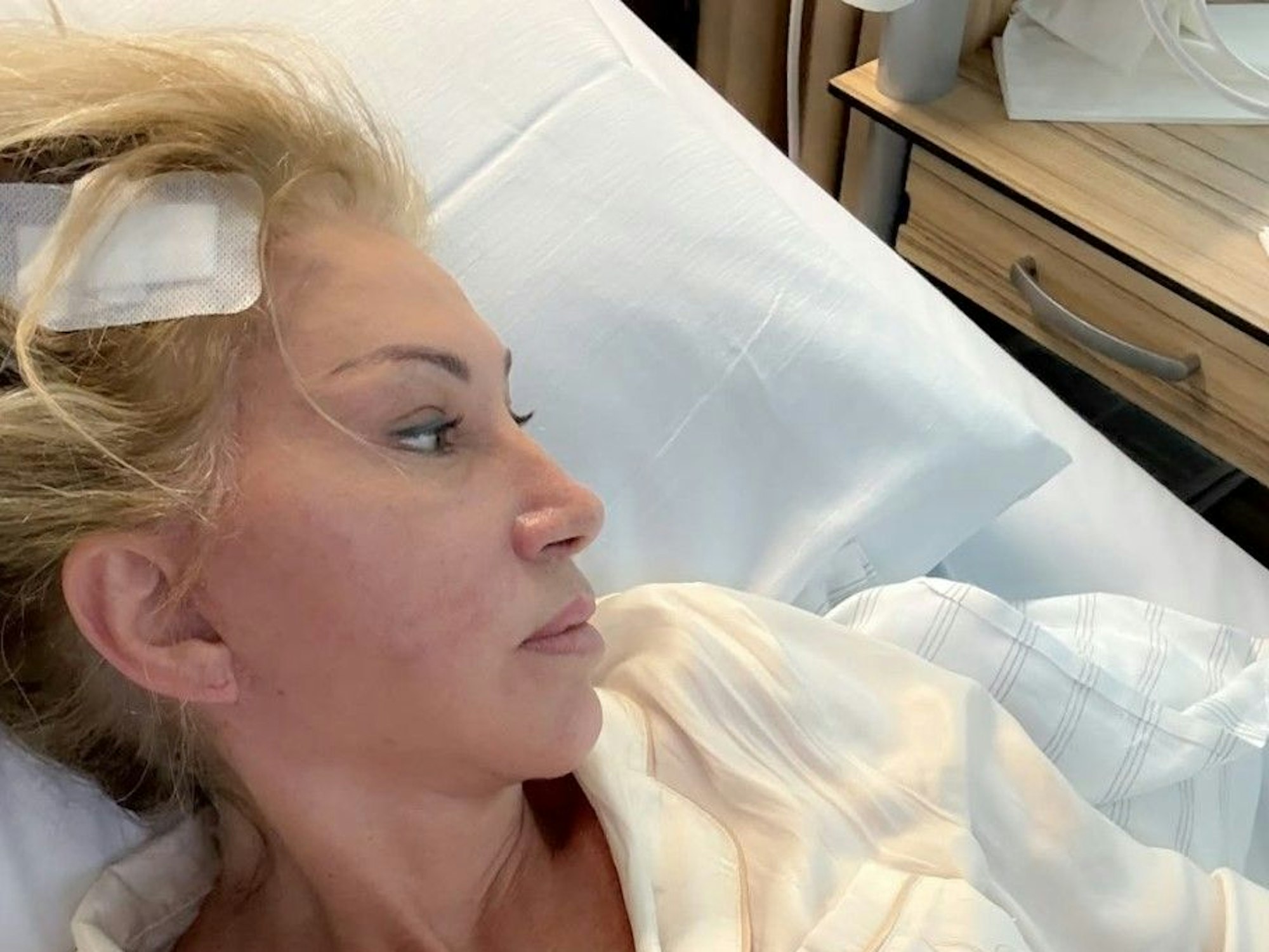 Carmen Geiss liegt mit einem Pflaster am Kopf in einem Krankenhausbett.