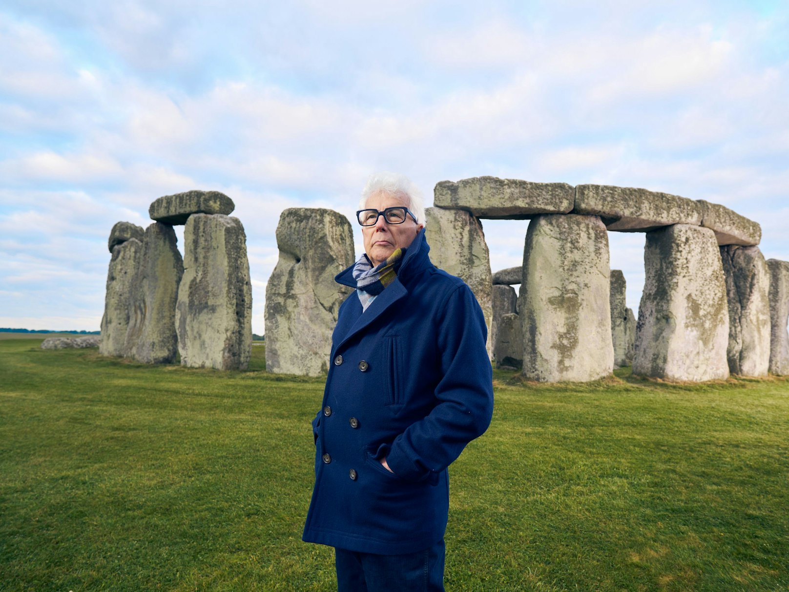 Ein Mann mit weißem Haar und schwarzer Brille steht vor dem Steinkreis in Stonehenge und blickt nachdenklich.