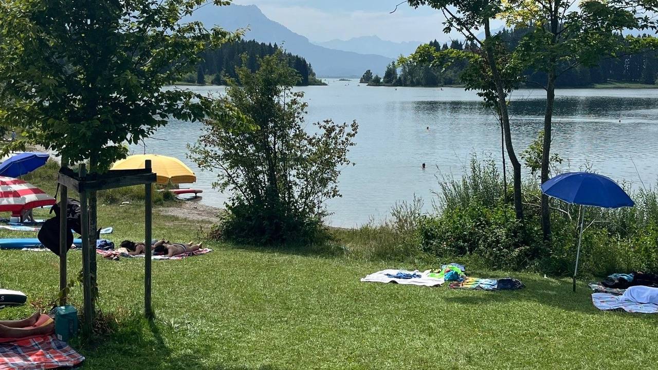Sonnenschirme auf einer Liegewiese an einem See vor einem atemberaubenden Bergpanorama.