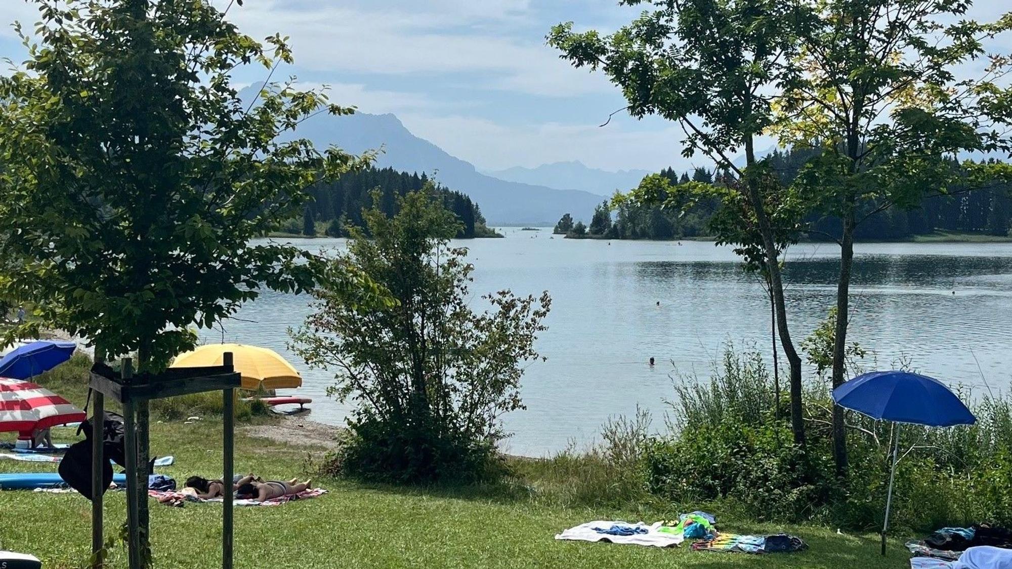 Sonnenschirme auf einer Liegewiese an einem See vor einem atemberaubenden Bergpanorama.