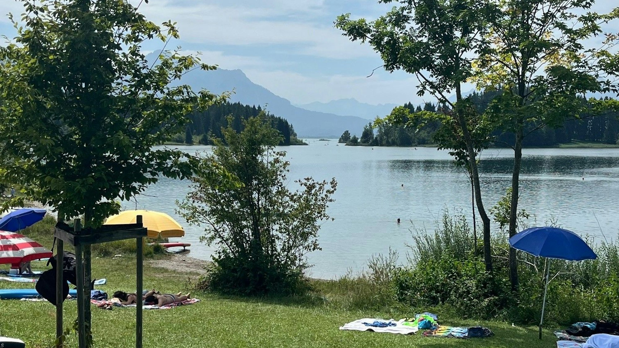 Sonnenschirme auf einer Liegewiese an einem See vor einem atemberaubenden Bergpanorama.