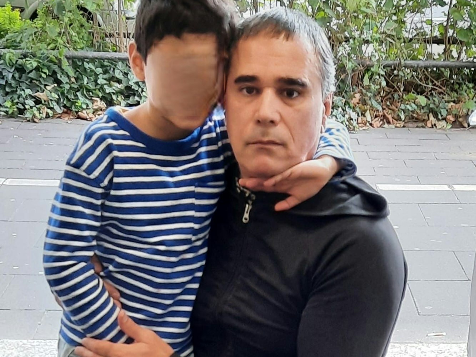Ein Junge umarmt seinen ernst guckenden Vater.