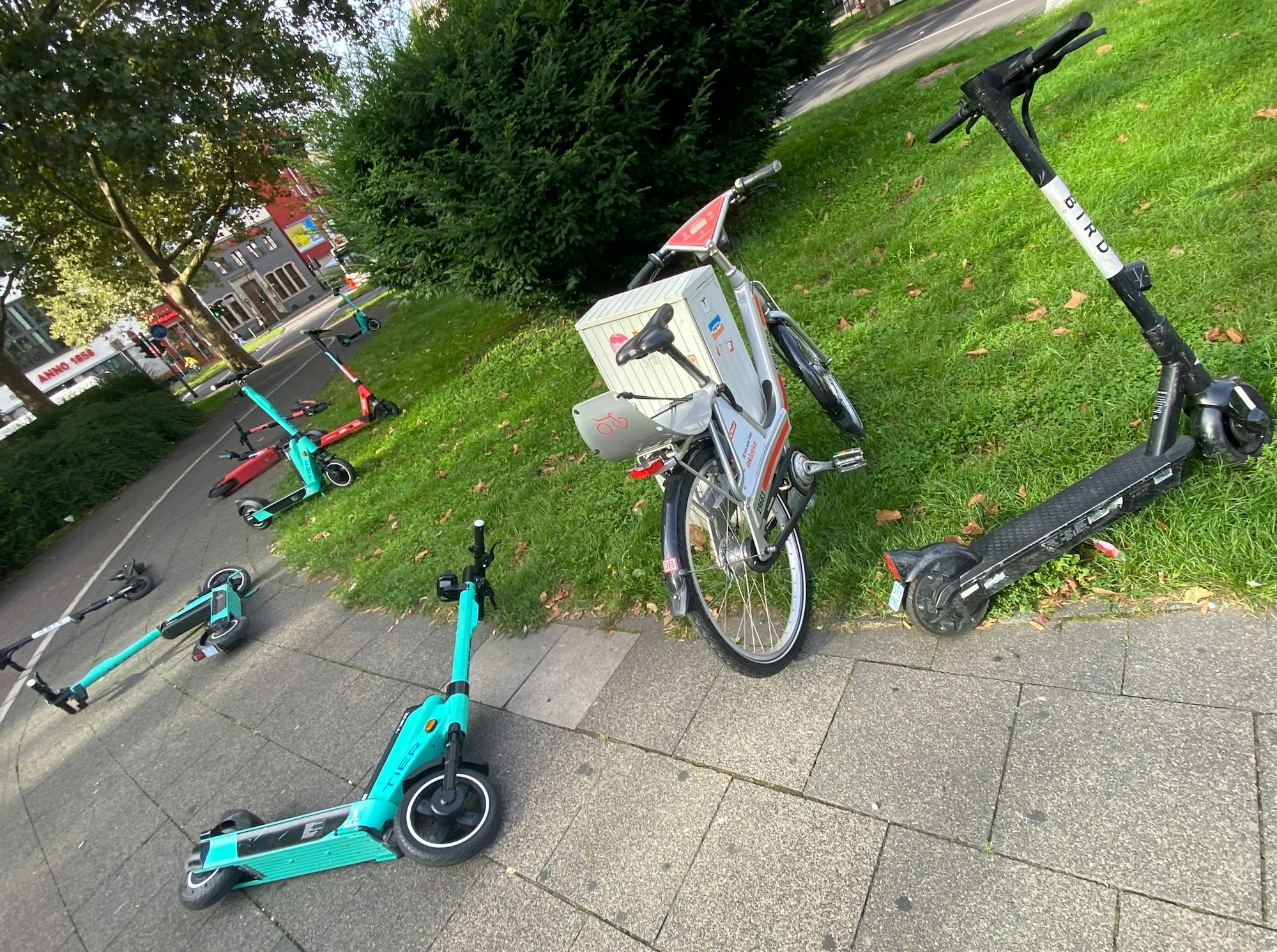 Mehrere E-Scooter stehen oder liegen auf einem Gehweg.