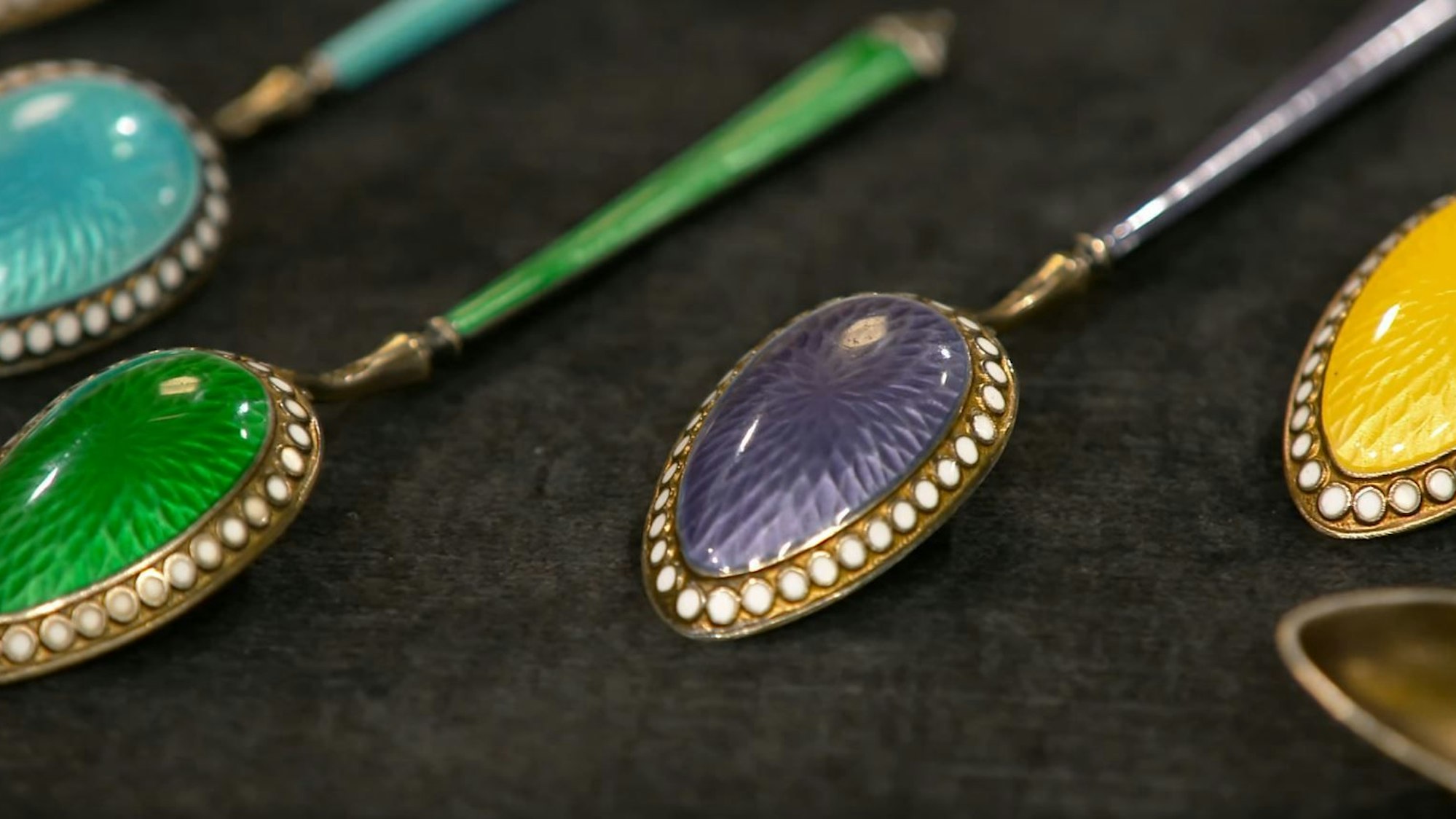 Sechs bunte Silberlöffel auf einem Tisch.