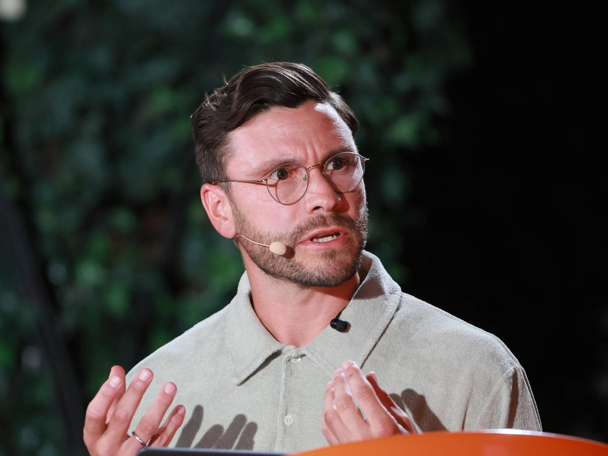 Jonas Hector trägt ein Mikro und spricht, während er mit beiden Händen gestikuliert.