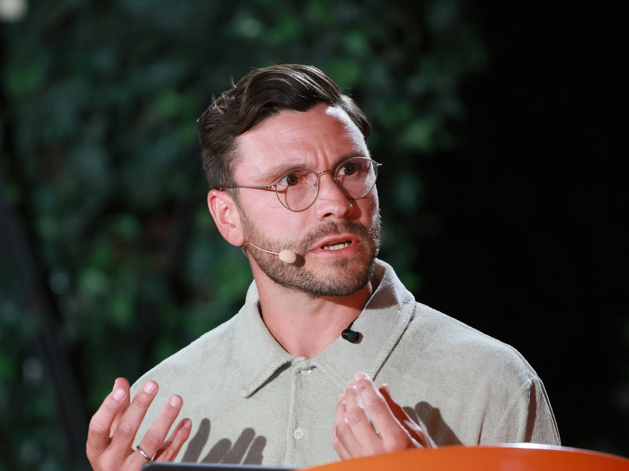 Jonas Hector trägt ein Mikro und spricht, während er mit beiden Händen gestikuliert.