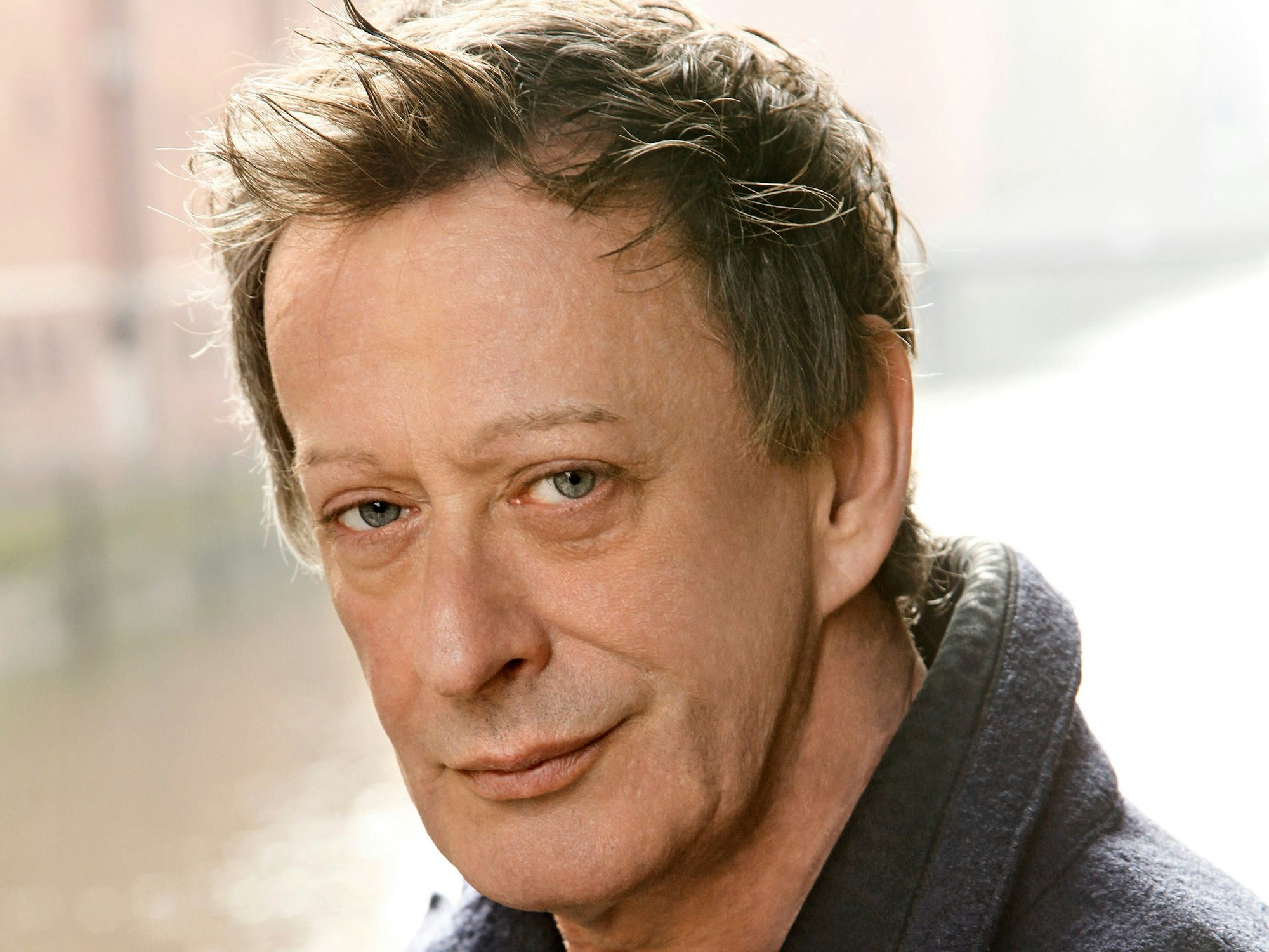 Ein Mann im blauen Mantel blickt nachdenklich in die Kamera.