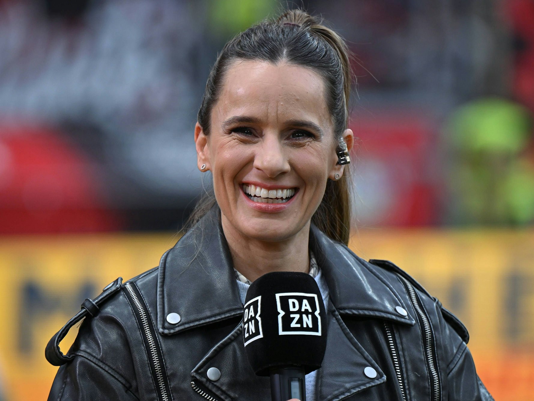 Christina Rann lacht mit DAZN-Mikrofon in der Hand.
