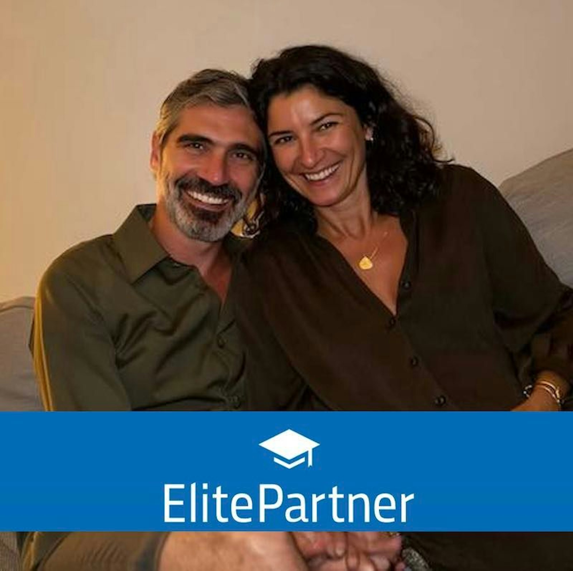 Eine Frau und ein Mann mittleren Alters sitzen lächelnd auf einer Couch nebeneinander und blicken in die Kamera.
