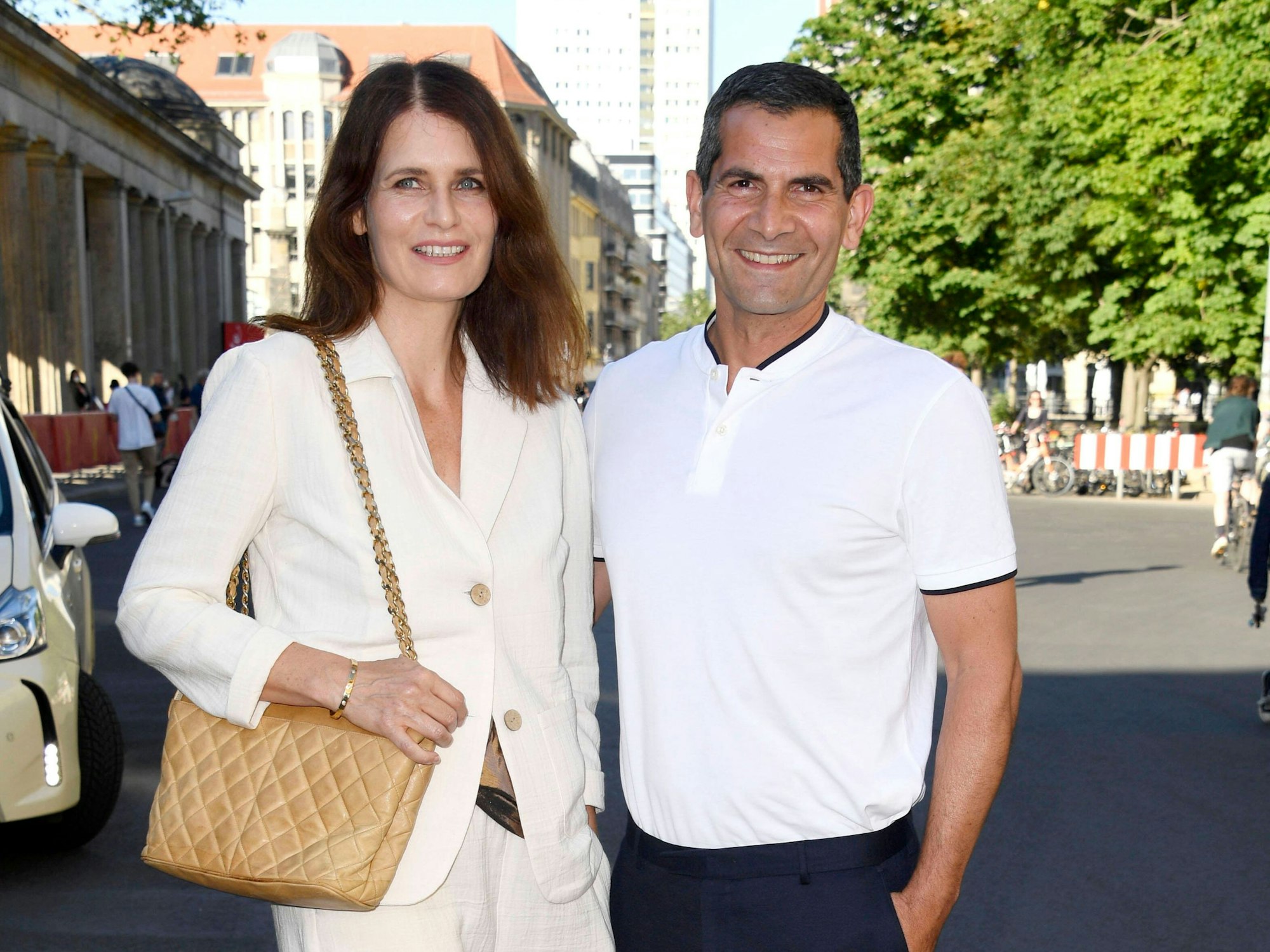 Ein Mann und eine Frau, beide sommerlich gekleidet, halten sich im Arm und lachen in die Kamera