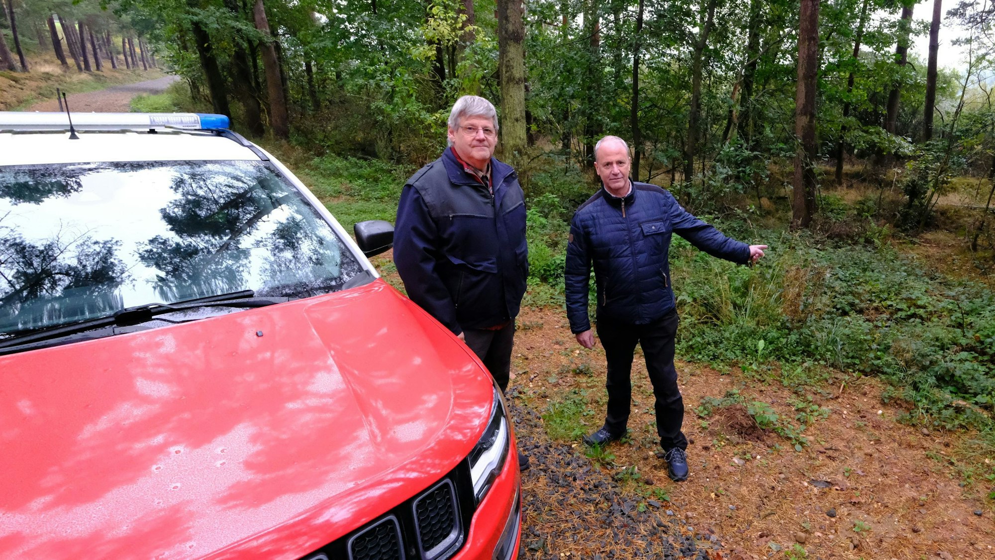 Zwei Männer im Wald neben einem Jeep am Fundort des gerissenen Rehs.