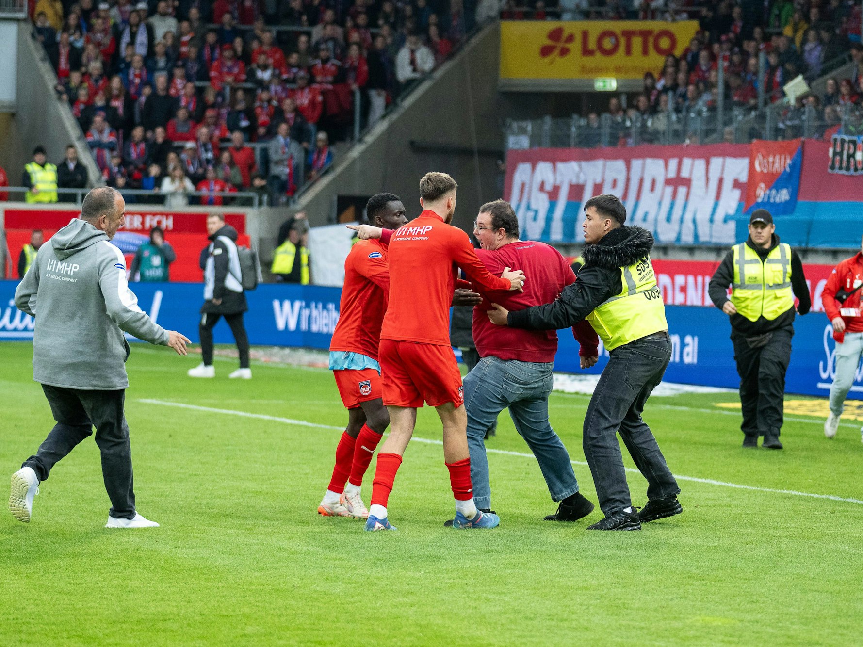 Security, Spieler und Trainer Frank Schmidt versuchen, einen erregten Fan zu beruhigen.