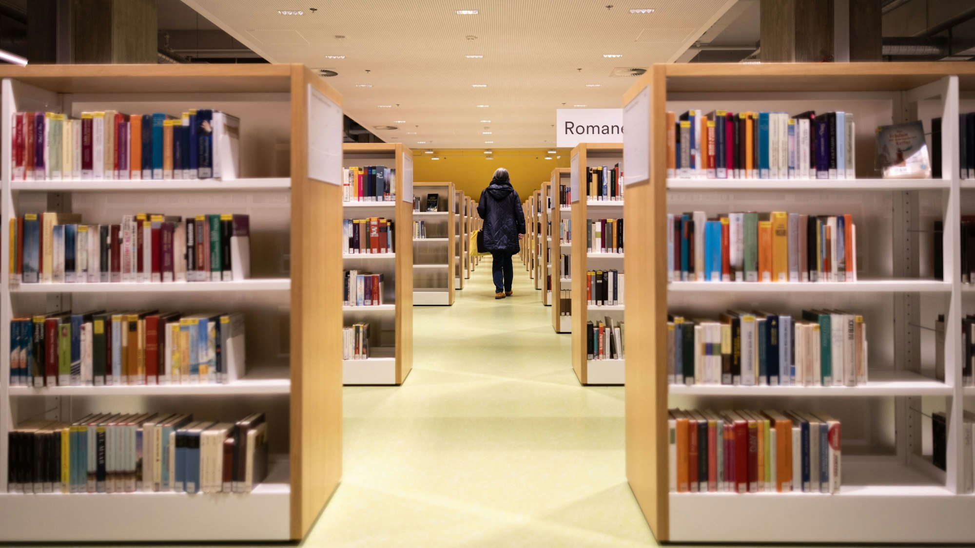 Eine Person geht zwischen Bücherregalen in der Zentralbibliothek der Stadt Düsseldorf umher.