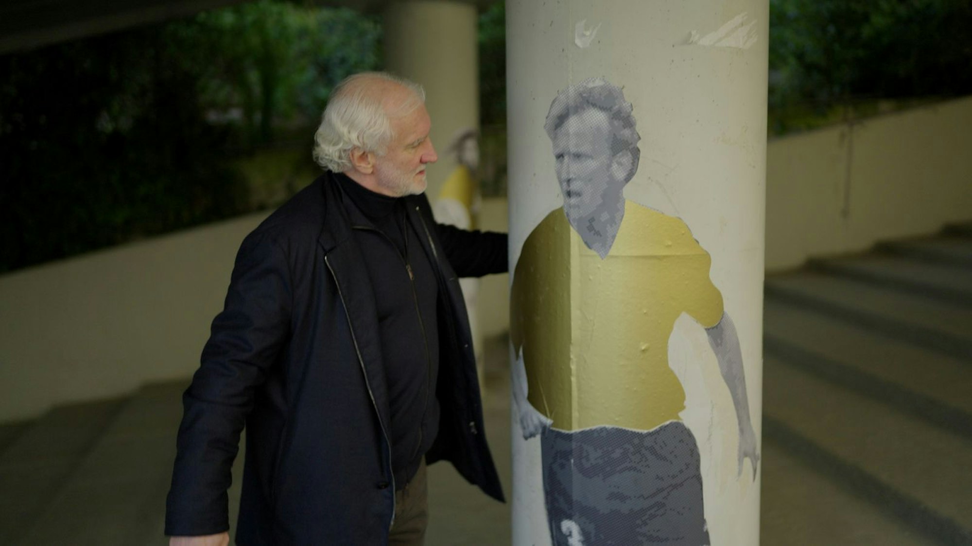 Emotionale Szene neben einem Stadiongemälde. Rudi Völler entdeckt ein Konterfei seines Freundes Andreas Brehme. Sein Mitspieler in der Weltmeister-Elf von 1990 war nicht nur Mannschaftskollege, sondern auch Völlers bester Freund. Im Februar 2024 ist Brehme - wie Völler 1960 geboren - überraschend verstorben. (Bild: © Sky/Banijay Productions Germany)