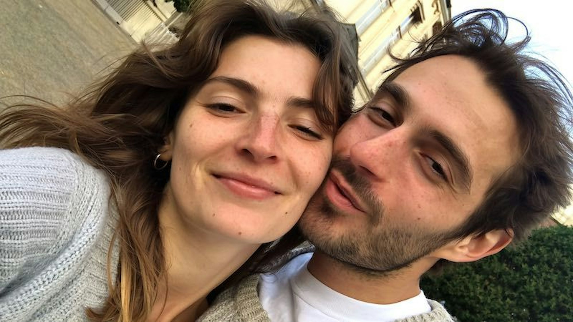 Ein Mann und eine Frau blicken fröhlich und verliebt in die Kamera und schießen ein Selfie.