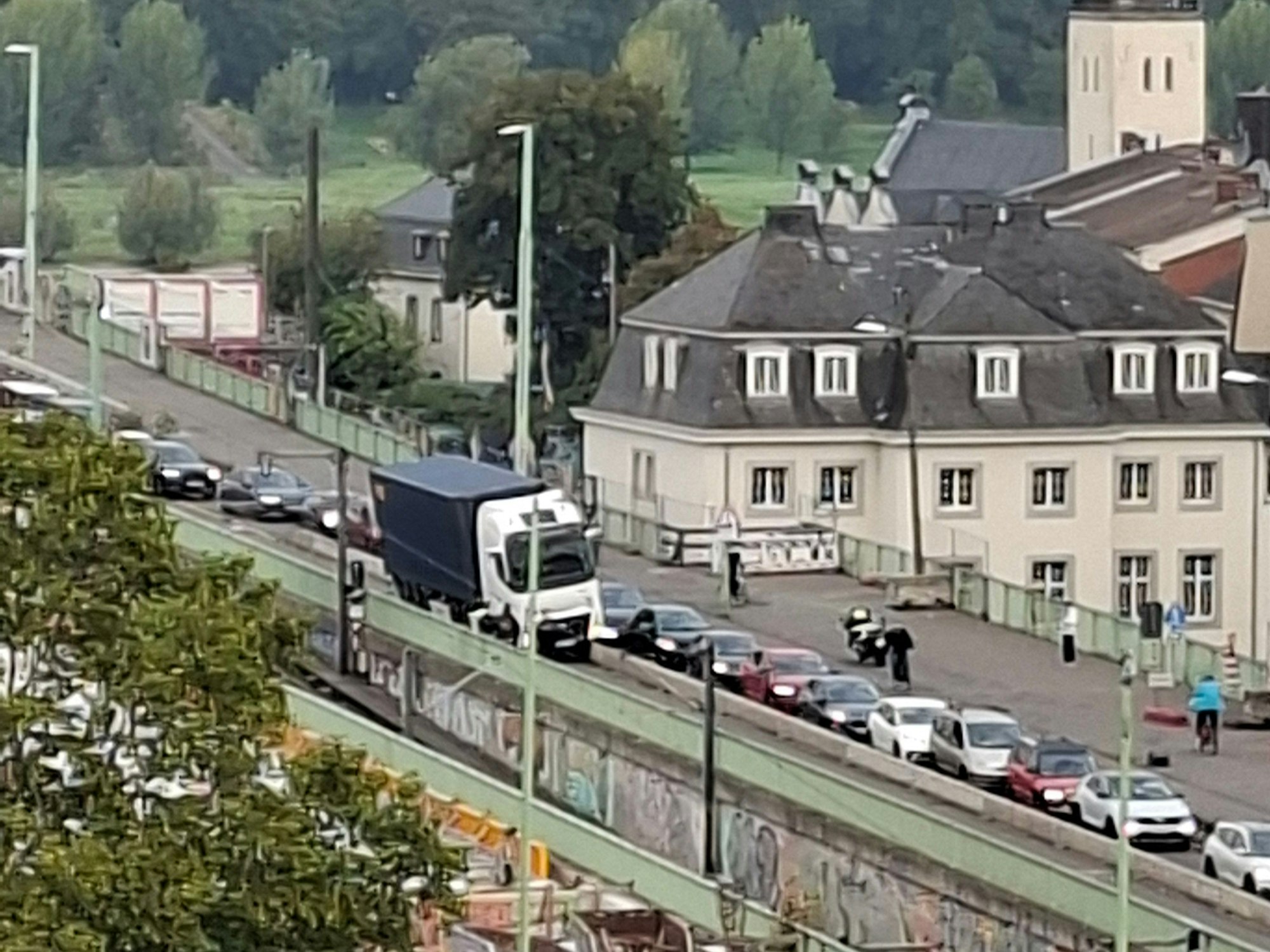 Ein Lkw hängt auf einer niedrigen Betonleitplanke fest, vor und hinter ihm staut sich der Verkehr.