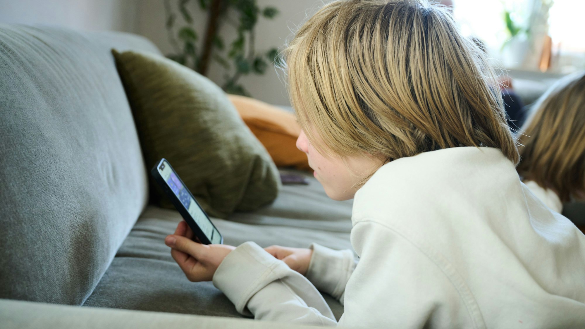 Ein Junge liegt auf einem Sofa und guckt auf sein Smartphone.
