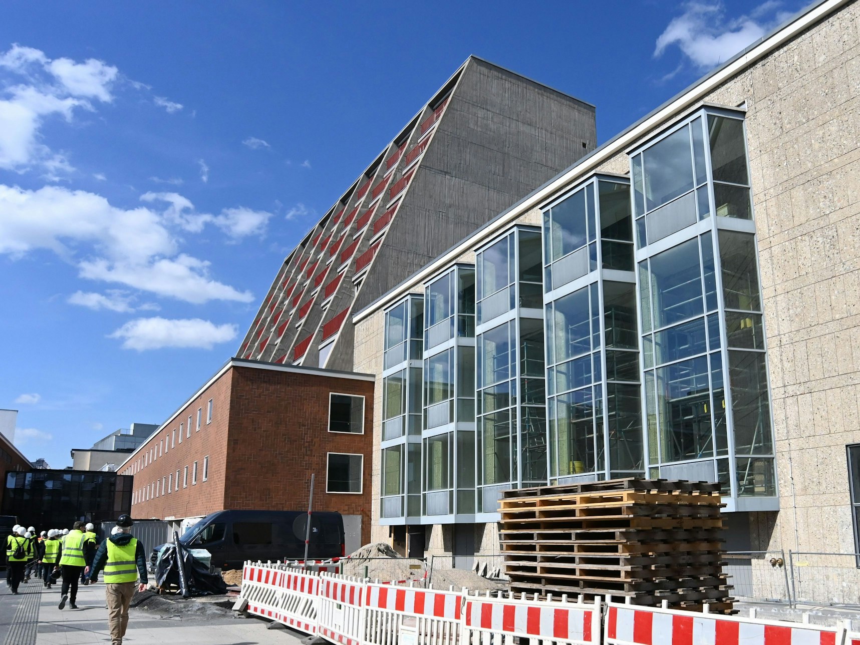 An der Kölner Oper stapeln sich Baumaterialien, ein Bereich ist mit Baustellenzäunen abgesperrt, mehrerer Arbeiter sind im Einsatz.