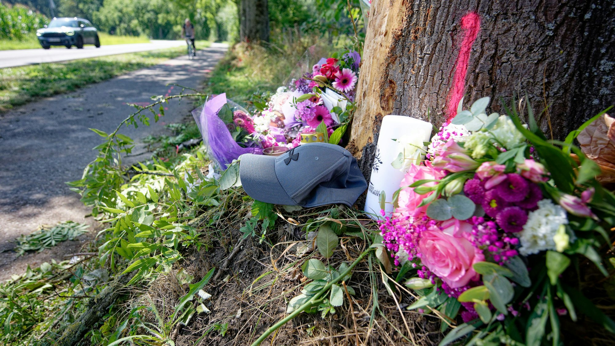 Blumen, Kerzen und eine Mütze liegen an am Fuße eines Baumstammes.