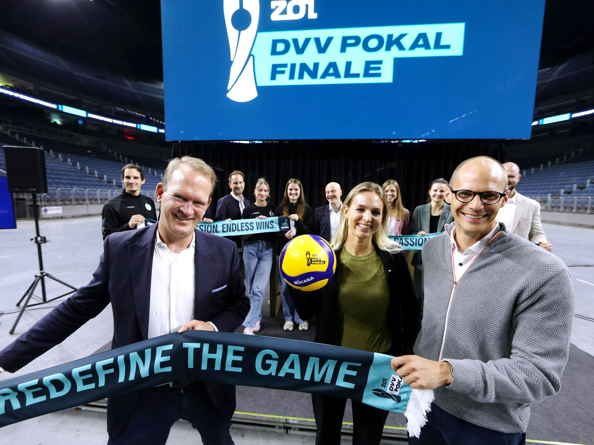 Stefan Löcher, Kim Oszvald-Renkema und René Beck halten einen Schal in die Kamera.