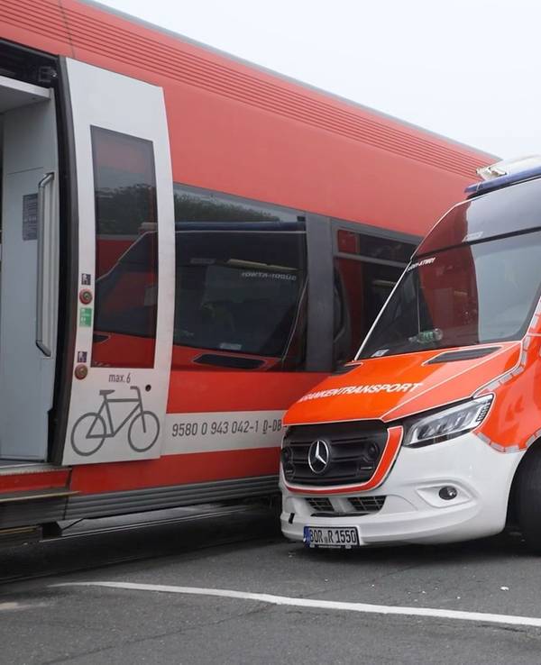 Ein Rettungswagen steht neben einem Regionalzug. Der Wagen ist an einem Bahnübergang mit dem Zug kollidiert.