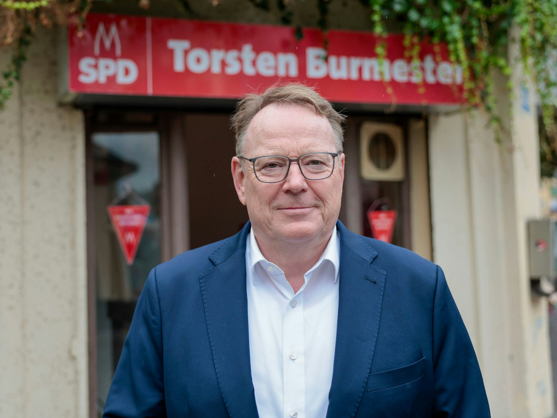 Ein Mann steht vor einem Eingang, über dem ein Schild mit der Aufschrift „SPD Torsten Burmeste“r hängt.