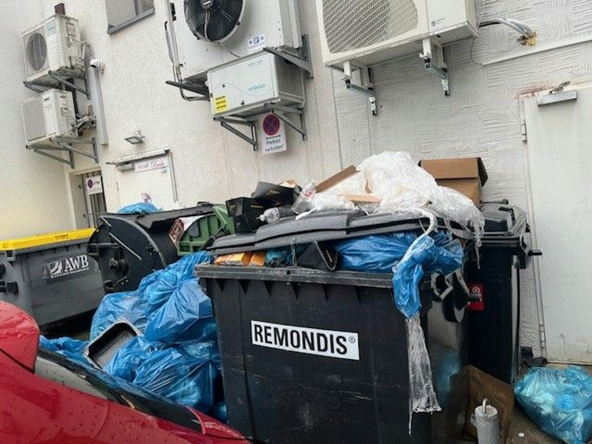 Ein Müllcontainer steht rappelvoll an einer Hauswand, um ihn herum stapeln sich Plastiksäcke.