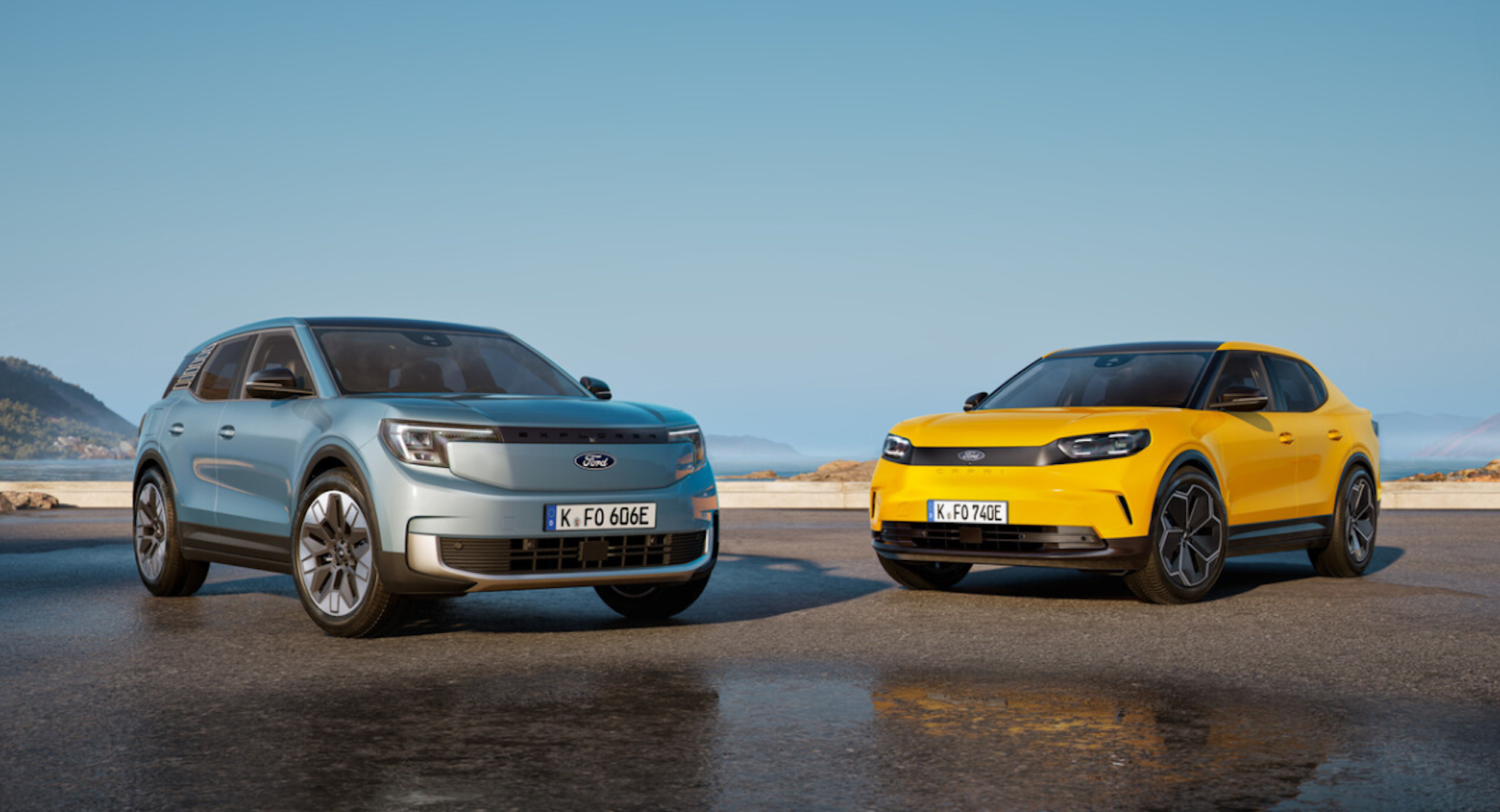 Das Foto zeigt zwei moderne vollelektrische SUVs von Ford, die nebeneinander auf einer nassen Straße am Meer stehen.