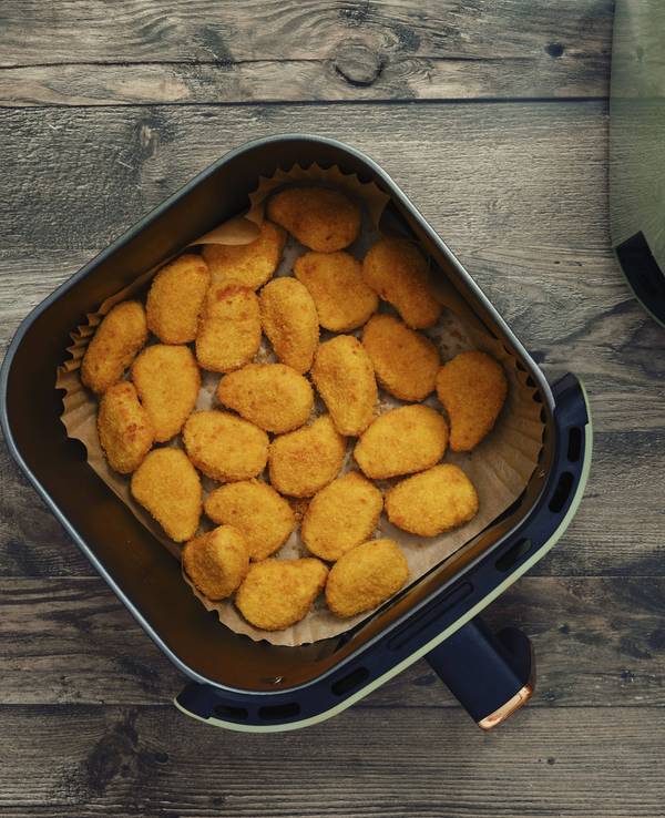 Goldene und knusprige Hähnchen Nuggets füllen den Korb einer Heißluftfritteuse.
