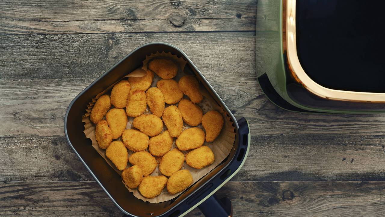 Goldene und knusprige Hähnchen Nuggets füllen den Korb einer Heißluftfritteuse.