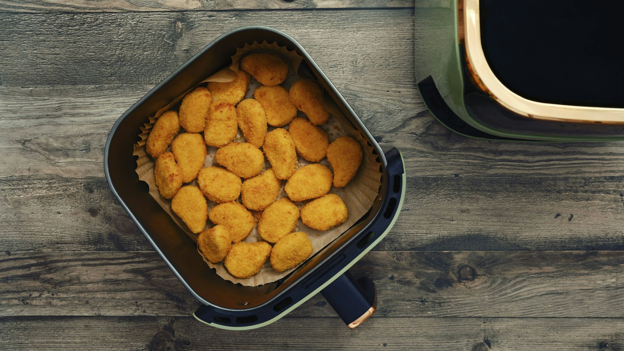 Goldene und knusprige Hähnchen Nuggets füllen den Korb einer Heißluftfritteuse.