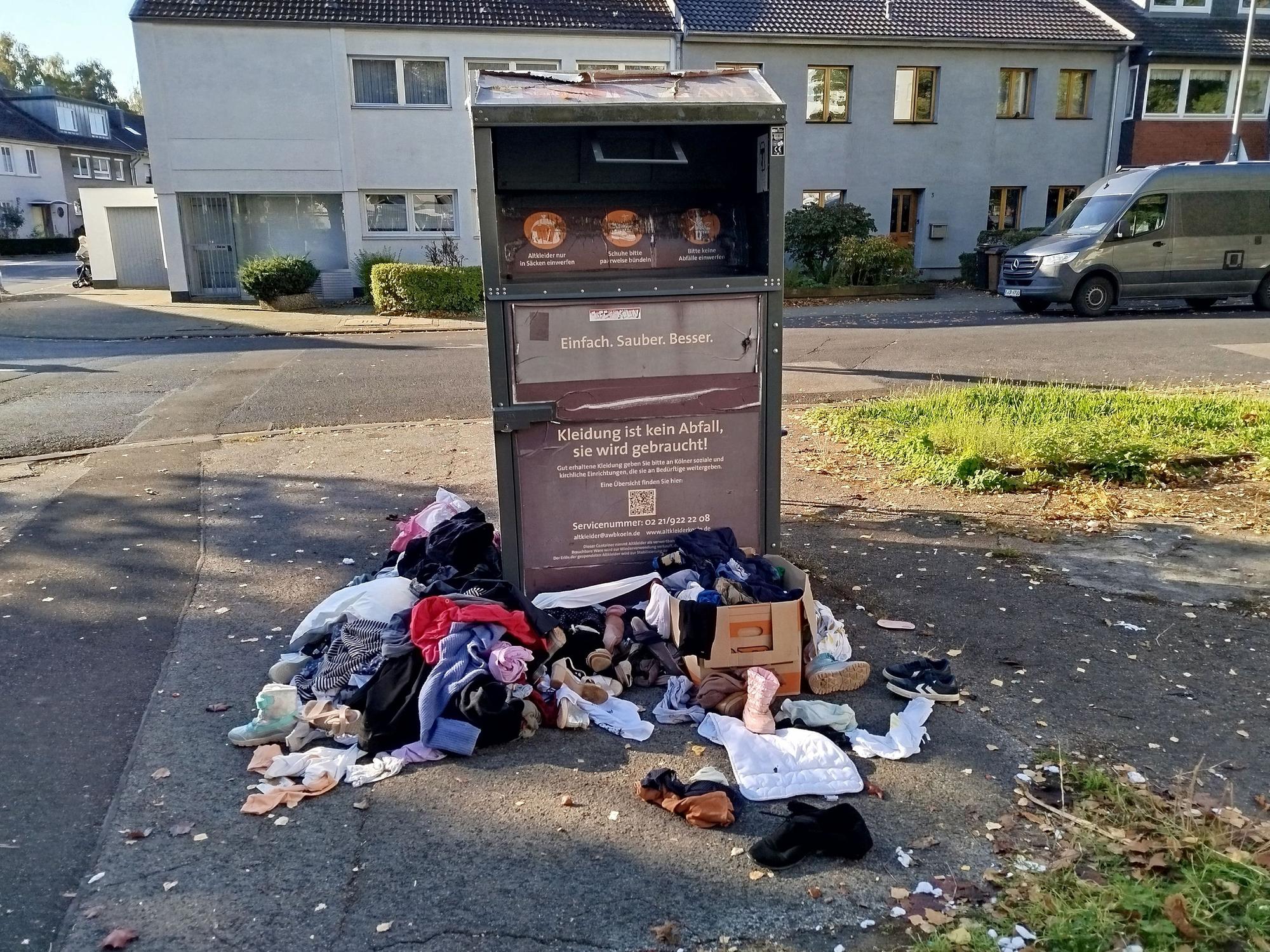Vor und neben einem Altkleidercontainer liegen Kleidungsstücke, Stofftiere, Kinderschuhe auf dem Boden.