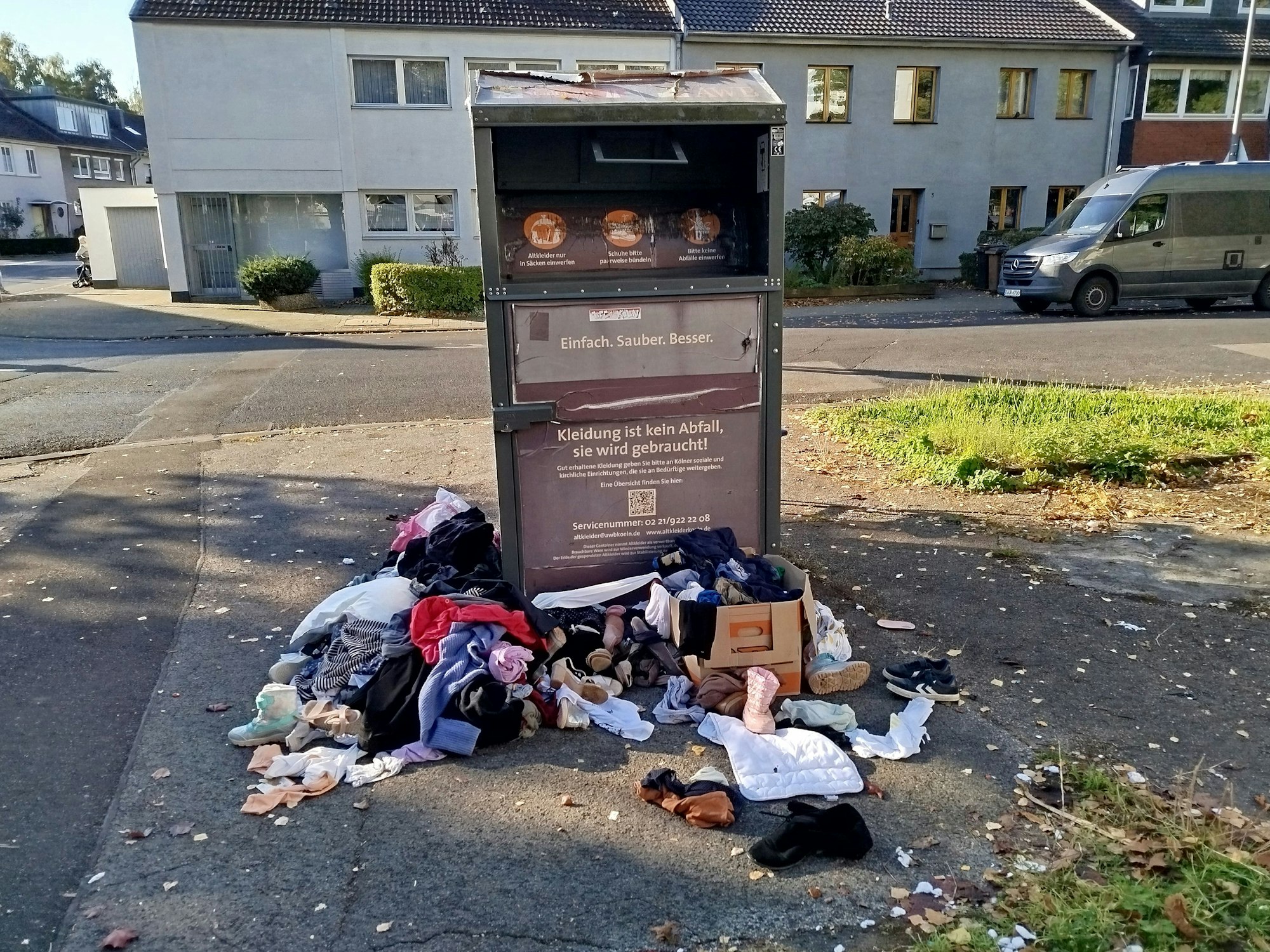 Vor und neben einem Altkleidercontainer liegen Kleidungsstücke, Stofftiere, Kinderschuhe auf dem Boden.