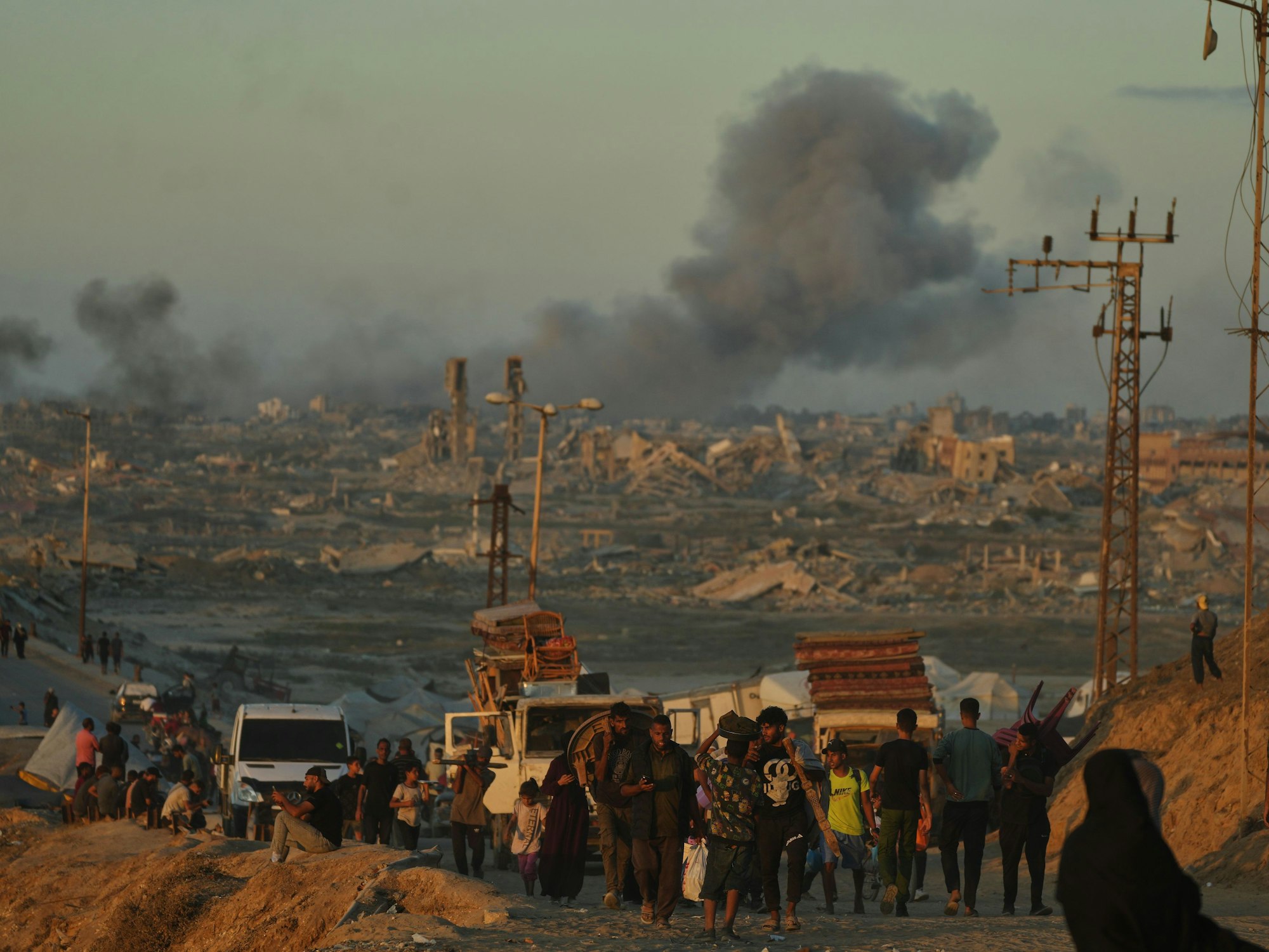 Menschen tragen Taschen, dahinter beladene Autos und aufsteigender Rauch.