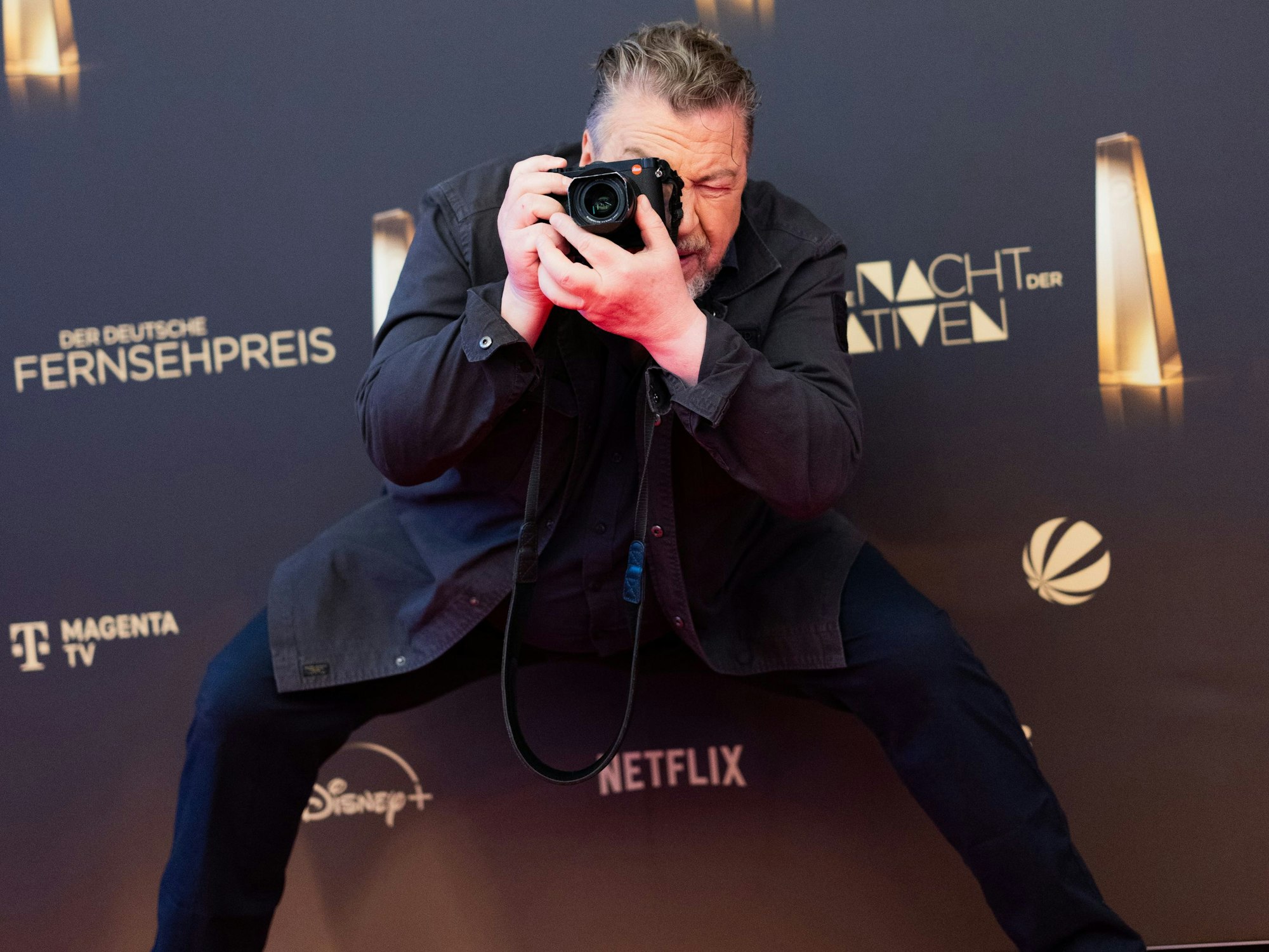 Ein Mann im dunklen Anzug steht vor einer Werbewand und macht Fotos.