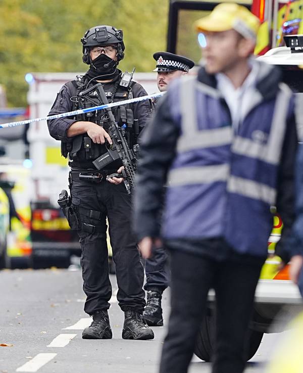 Bewaffnete Polizeibeamte stehen hinter iner Absperrung.