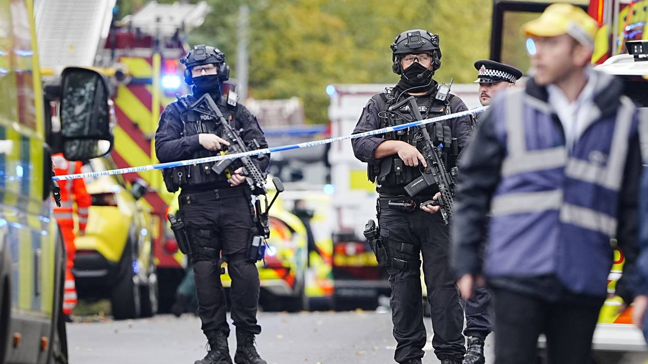 Bewaffnete Polizeibeamte stehen hinter iner Absperrung.