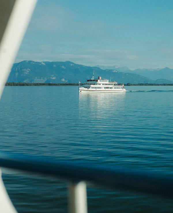 Ein weißer Ausflugsdampfer fährt über einen tiefblauen See vor einer Gebirgssilhouette vorbei.