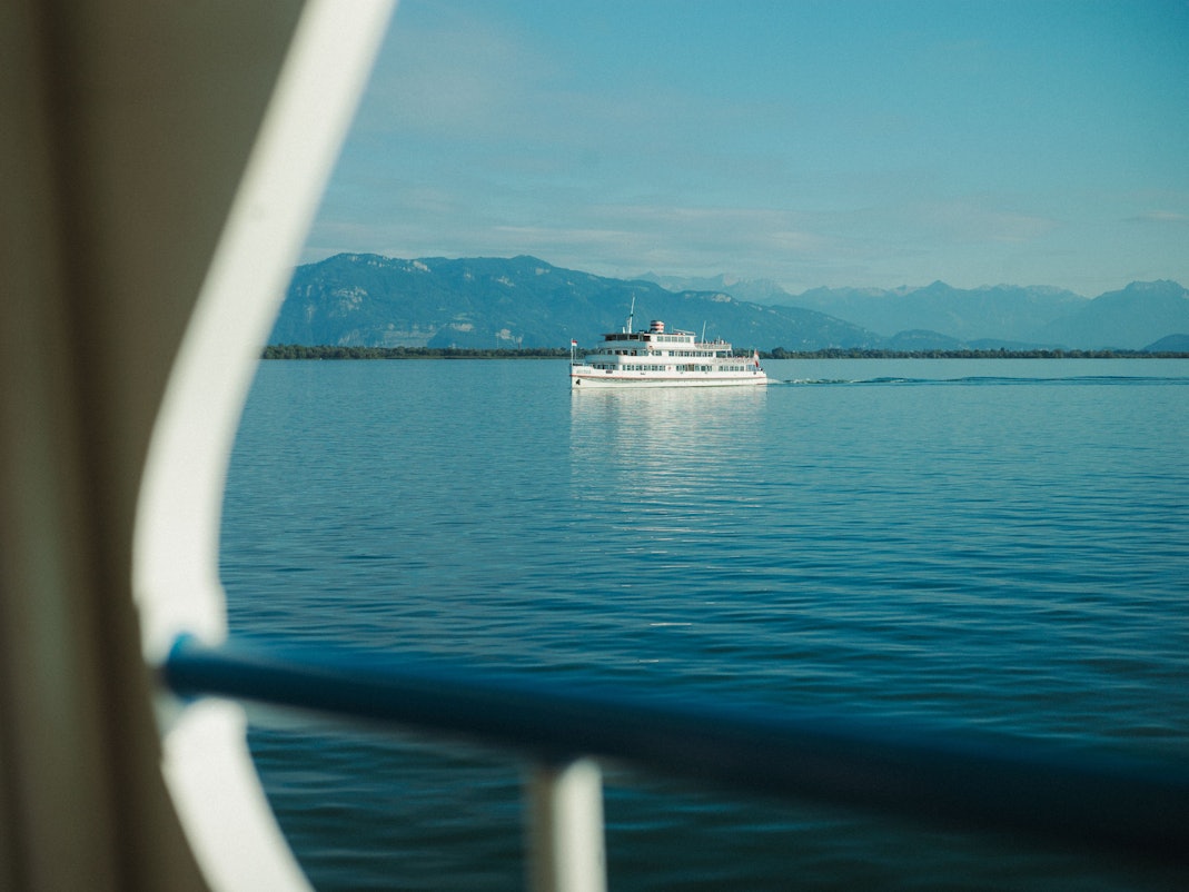 Ein weißer Ausflugsdampfer fährt über einen tiefblauen See vor einer Gebirgssilhouette vorbei.