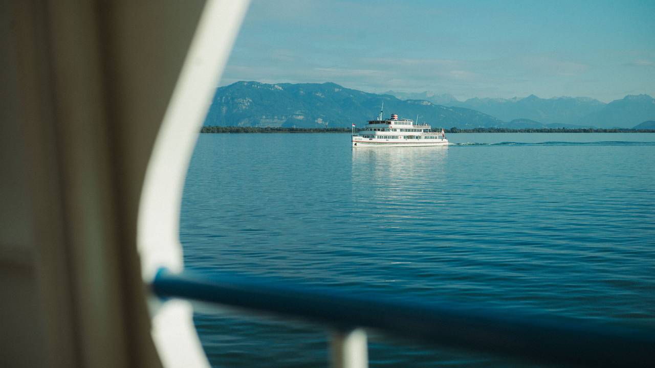 Ein weißer Ausflugsdampfer fährt über einen tiefblauen See vor einer Gebirgssilhouette vorbei.